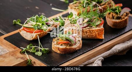 Bannière alimentaire. Bruschettas et canapés avec pate de dinde et microgreens sur une planche à découper. Cuisine méditerranéenne traditionnelle. Délicieux petit déjeuner maison Banque D'Images