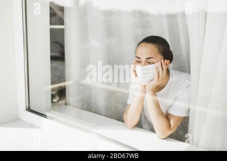 Médecin fatigué dans le masque médical regardant par la fenêtre. Travail important et auto-isolement pendant la pandémie de coronavirus. Espoir pour la médecine. Banque D'Images