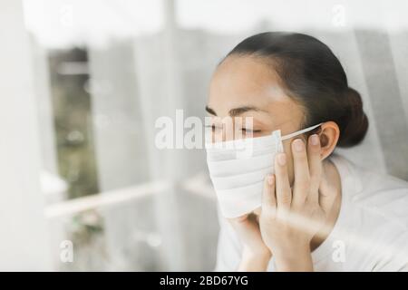 Médecin fatigué dans le masque médical regardant par la fenêtre. Travail important et auto-isolement pendant la pandémie de coronavirus. Espoir pour la médecine. Banque D'Images