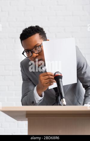 un orateur afro-américain effrayé se cache derrière le papier lors de la conférence des entreprises Banque D'Images