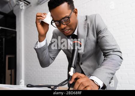 frustré, sueur de haut-parleur afro-américain avec serviettes de table lors d'une conférence d'affaires avec microphone Banque D'Images