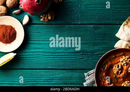 Plat moyen-oriental. Tartiner de poivron rouge rôti - muhammara - dans un bol rouge sur fond de bois bleu-vert avec divers ingrédients Banque D'Images