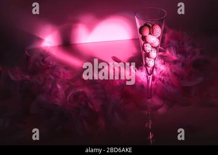 Œufs Quail dans flûte de champagne avec plumes sur fond brillant. La vie créative en couleur rose. Concept de Pâques. Banque D'Images
