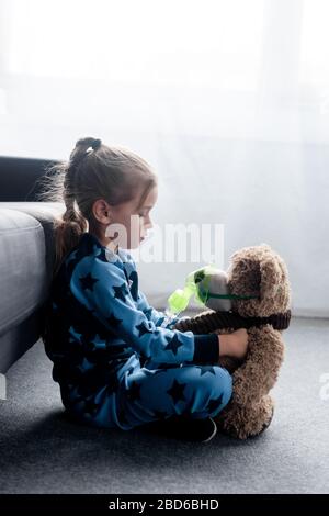 vue latérale de l'enfant mignon tenant un ours en peluche dans le masque respiratoire Banque D'Images