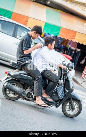 Deux jeunes étudiants cambodgiens se précipitent dans les rues animées de Phnom Penh avec le passager concentré sur son téléphone portable. Banque D'Images