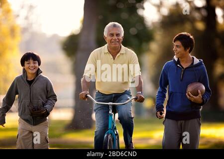 Smiling senior man having fun riding a bicycle tandis que dans un parc avec ses deux petits-fils. Banque D'Images