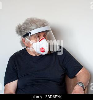 Senior avec masque antiviral de protection FFP3 et casque de protection contre le coronavirus. Homme caucasien à poil blanc dans un T-shirt noir sur wal blanc Banque D'Images