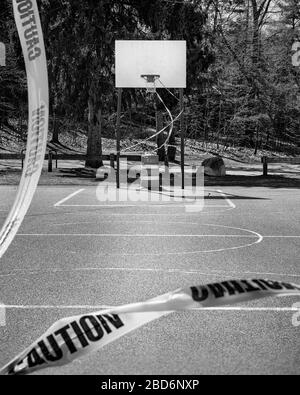 Un terrain de basket-ball extérieur est fermé à COVID-19 (Coronavirus). Le panier est dégarni par un ruban de mise en garde jaune vif et un pilon. De la vue Banque D'Images