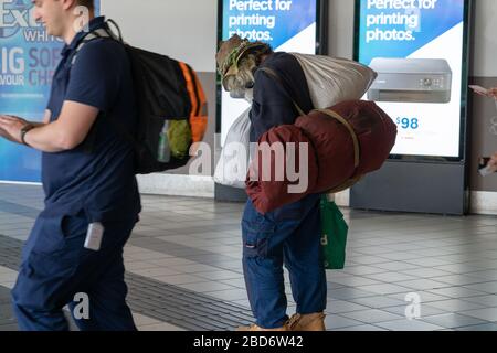 Melbourne Australie - 10 mars 2019 ; homme principal portant des sacs portant de vieux chapeau marche le long du sentier de randonnée devant des panneaux publicitaires. Banque D'Images