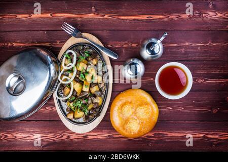 Kuurdak - plat de viande traditionnel fabriqué en Asie centrale. Servir sur une poêle chaude avec une mouture de poivre, du pain standard et du thé. Vue de dessus Banque D'Images