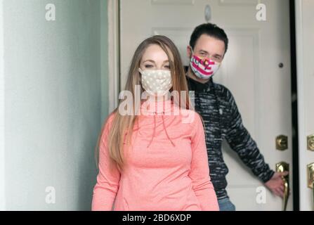 Un jeune couple portant un masque de visage lors de sortir de sa maison. Le gouvernement conseille aux gens de porter des masques en tissu pour se protéger contre le covid-19 Banque D'Images