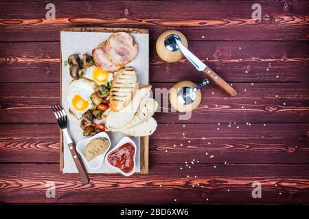 Grand petit déjeuner. Jambon, pain grillé, œufs frits, champignons grillés et tomates avec sauce. Il y a un moulin à poivre et des couverts. Vue de dessus Banque D'Images