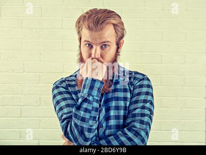Réflexion. Portrait d'un homme inquiet décontracté chemise bleue homme regardant votre appareil photo isolé mur de briques blanches arrière-plan. Image jaune, horizontale. Banque D'Images