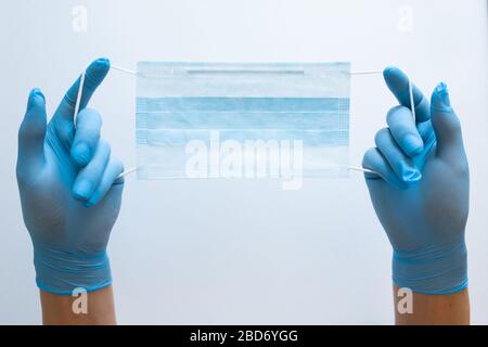 Vue de la première personne d'une femme tenant un masque facial sur un fond de table blanc. Masque de protection pour la propagation du virus. Gros plan, espace de copie, vue de dessus, plat. Banque D'Images