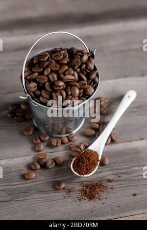 Grains de café Arabica dans un petit seau miniature. Café moulu dans une cuillère en céramique blanche sur fond en bois Banque D'Images