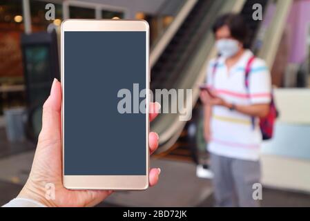 Gros écran vide de téléphone mobile dans la main de la femme avec l'homme flou portant le masque de visage pour empêcher l'infection dans le fond Banque D'Images