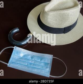 Sur une surface en bois sombre, nous avons un chapeau de paille pour homme, la poignée d'un parapluie et un masque médical de protection. Banque D'Images