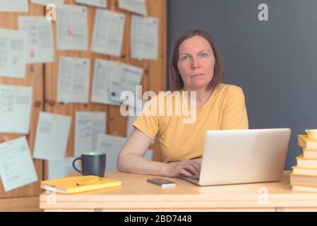 Traductrice indépendante féminine réfléchie travaillant au bureau à domicile avec ordinateur portable et smartphone, mise au point sélective Banque D'Images