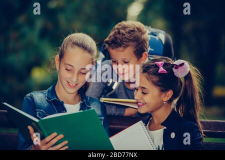 Retour à l'école. Les enfants avec des sacs à dos ont du plaisir, de parler, de lire un livre.Groupe d'écoliers élémentaires ayant une discussion sur les devoirs pendant leur déplacement Banque D'Images