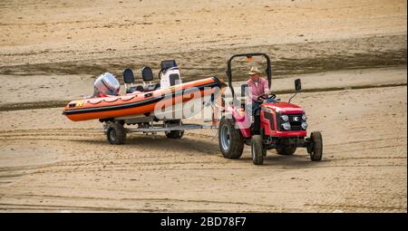 TENBY, PEMBROKESHIRE, PAYS DE GALLES - AOÛT 2018 : tracteur remorqueur d'une remorque avec un bateau à vitesse gonflable dans le port de Tenby, dans l'ouest du pays de Galles à marée basse Banque D'Images
