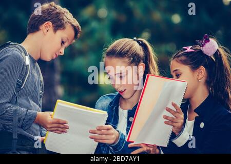 Retour à l'école. Les enfants avec des sacs à dos ont du plaisir, de parler, de lire un livre.Groupe d'écoliers élémentaires ayant une discussion sur les devoirs pendant que goi Banque D'Images