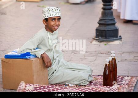 Un adolescent souriant se trouve sur le sol et vend du miel sur le marché du vendredi dans l'ancien souk de Nizwa en Oman Banque D'Images