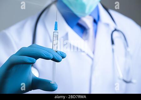 Médecin en masque de gaze et seringue de maintien de la robe médicale dans son gant bleu en latex vêtu de la main. Concept de santé et de vaccination Banque D'Images