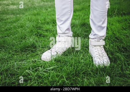Pieds mâles en chaussures blanches sur l'herbe verte. Jeans blancs. Banque D'Images