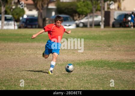 Jeune joueur de football en uniforme bleu rouge kicking football ball dans le parc Banque D'Images