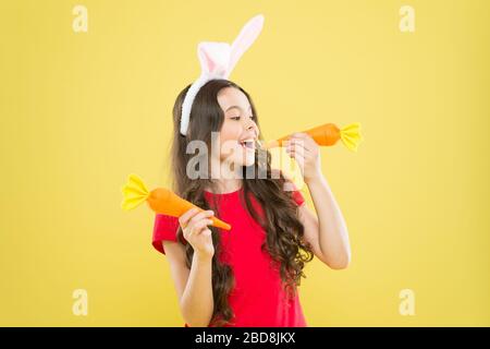 petite fille heureuse nourriture pour lapins. enfance en bonne santé. bonne pour vos dents. Grignotez une carotte comme un lièvre. Les enfants dans les oreilles de lapin aiment manger de la carotte. Costume de lapin enfant avec carotte. Banque D'Images