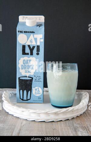 Boisson au lait d'avoine végan Oatly en verre bleu vintage avec le carton de boisson d'avoine Oatly original derrière sur plateau blanc avec fond noir. Utilisation Editoral onl Banque D'Images