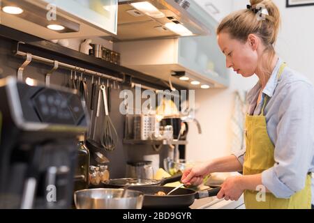 Restez chez la femme au foyer en cuisine, en sautant dans une casserole, en préparant la nourriture pour le dîner en famille. Banque D'Images