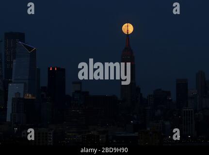 New York, États-Unis. 7 avril 2020. Une Supermoon rose monte derrière l'Empire State Building et la ville de Manhattan avec un éclairage éclairé en rouge pour honorer les travailleurs d'urgence qui combattent le coronavirus le mardi 7 avril 2020. A travers la bataille de COVID-19, les feux blancs signature sur l'ESB ont été remplacés par le battement de coeur de l'Amérique ainsi qu'une sirène blanche et rouge dans le mât pour les travailleurs héroïques d'urgence sur la ligne de front de la lutte." Photo de John Angelillo/UPI crédit: UPI/Alay Live News Banque D'Images