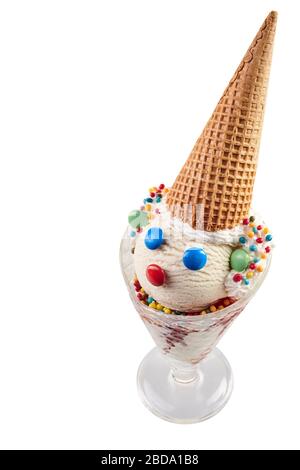 Verre de crème glacée blanche avec un visage clown fait de chocolats à boutons colorés et de cône de gaufres comme un chapeau, vu de grand angle et isolé sur le whi Banque D'Images