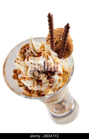 Vue en haut sur un tourbillon de glace à la vanille parsemée de noix assorties et garnie de spirales de chocolat et de biscuits dans un grand verre isolé sur Banque D'Images