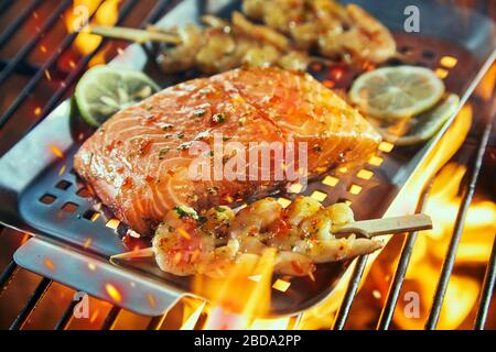 Filet de saumon cru avec des kebabs de crevettes assaisonnés de piment et d'épices sur une cuisson au feu dans une griddle au-dessus de la grille en gros plan avec des tranches de citron Banque D'Images