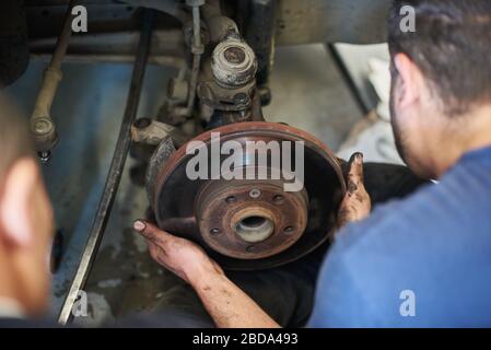 Gros plan sur les mains mâles tenant le disque de la roue automobile. Homme prenant soin de la roue de voiture en cours de remplacement de pneu neuf dans le garage. Concept de service automatique. Banque D'Images