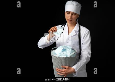 Le médecin tient un seau rempli de masques faciaux usagés, les jetant comme symbole de fin d'épidémie Banque D'Images