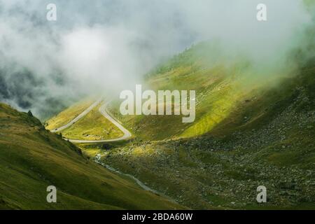 La route qui traverse les montagnes de Fagaras vues d'en haut parmi le brouillard, Transfagarasan, Roumanie Banque D'Images