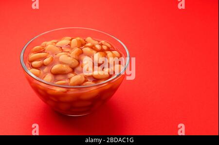 Haricots cuits dans la sauce tomate isolés sur fond rouge Banque D'Images