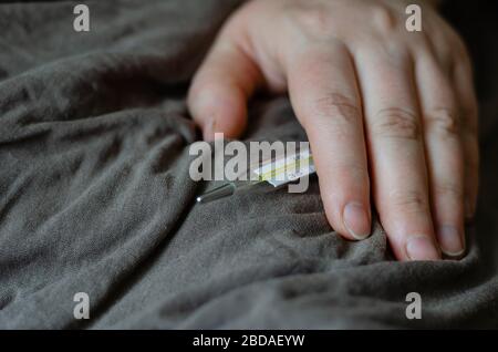 La main féminine repose sur une couverture. Dans sa main est un thermomètre au mercure. Le concept est le repos du lit, le traitement, la mesure de la température. Prise de vue au niveau des yeux. Banque D'Images