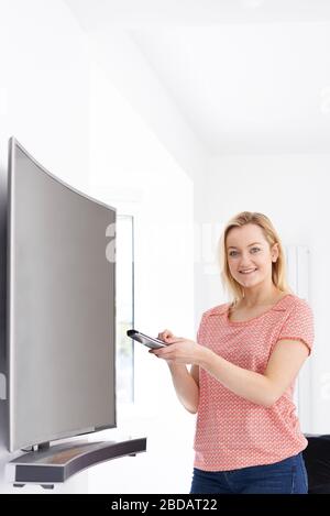 Portrait de la jeune femme avec une nouvelle télévision à écran incurvé à la maison Banque D'Images