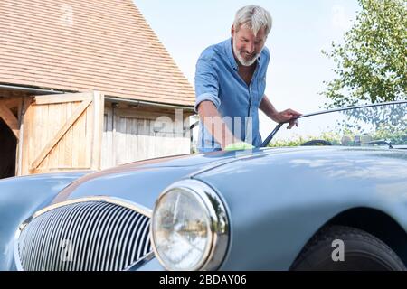 Homme mature restauré Polissage Voiture de sport classique dehors à la maison Banque D'Images