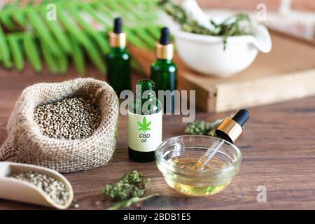 Bouteilles d'huile de chanvre avec graines de cannabis et feuilles sèches sur table en bois blanc. Huile médicale CBD. Concept de médecine alternative. Banque D'Images