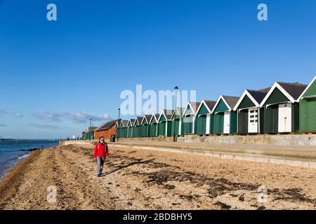 Personne marchant devant les huttes de plage, Gurnard, île de Wight, Royaume-Uni Banque D'Images