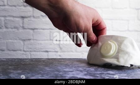 Une main masculine a levé ou met un masque médical blanc sur une table grise contre un mur de briques blanches avec espace de copie. Masques médicaux pendant les éclosions de di viral Banque D'Images