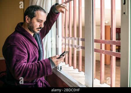 homme regardant dans la fenêtre et utilisant le smartphone Banque D'Images