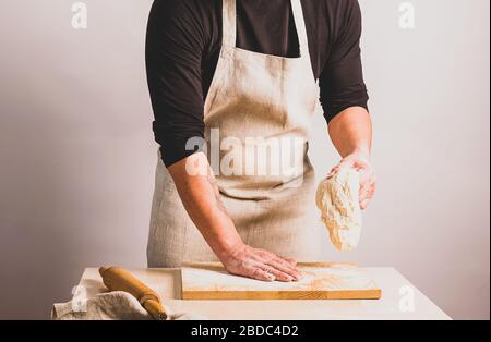 Un homme dans un tablier pétrit la pâte fait du pain. Le concept de la pâtisserie maison. Mise au point sélective. Banque D'Images