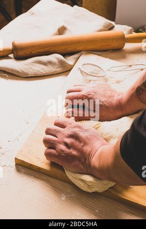 Un homme dans un tablier pétrit la pâte fait du pain. Le concept de la pâtisserie maison. Mise au point sélective. Cadre vertical. Banque D'Images