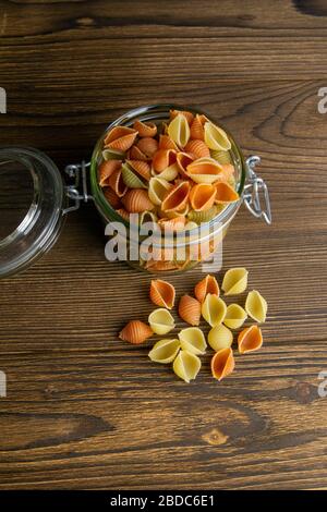 Pâtes Conchiglie colorées dans un pot en verre sur fond en bois. Vues de face, gros plan Banque D'Images